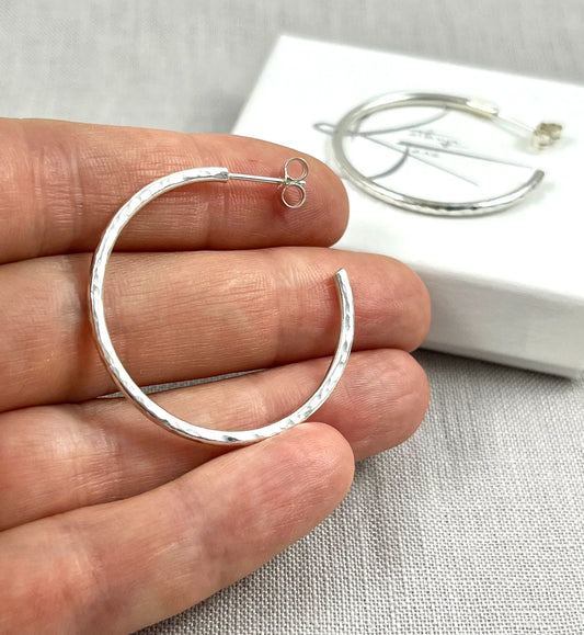 Hand holding medium hammered silver hoop stud earring with textured finish