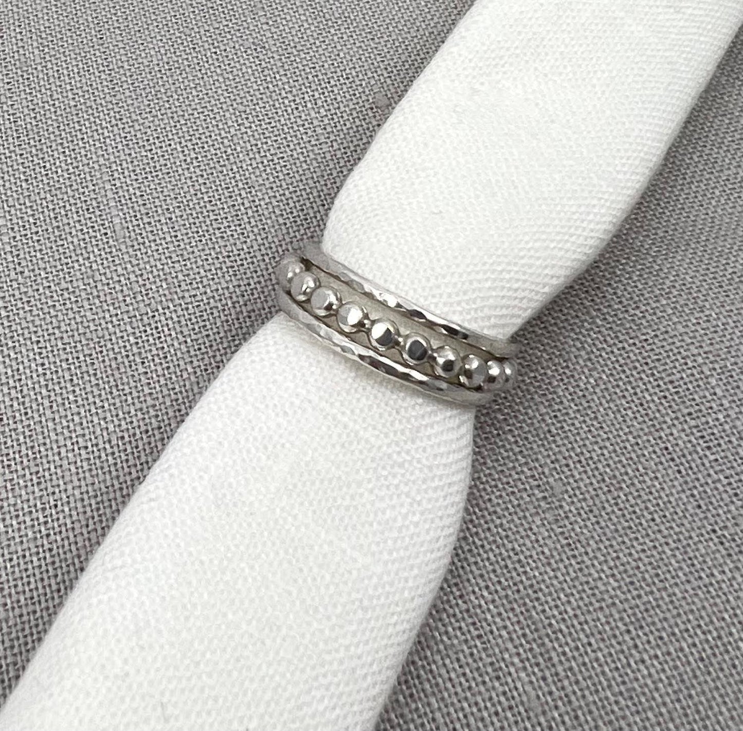Sterling silver beaded ring with hammered edges on white fabric background