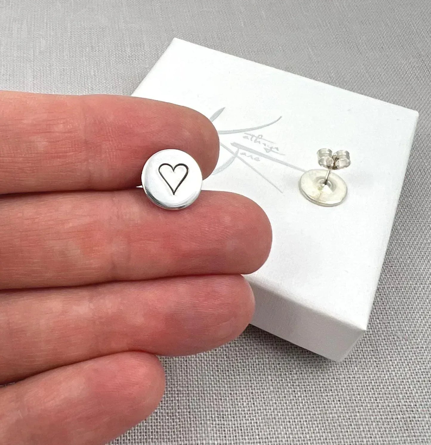 Sterling silver heart stud earrings displayed on hand and white box, minimalist jewelry
