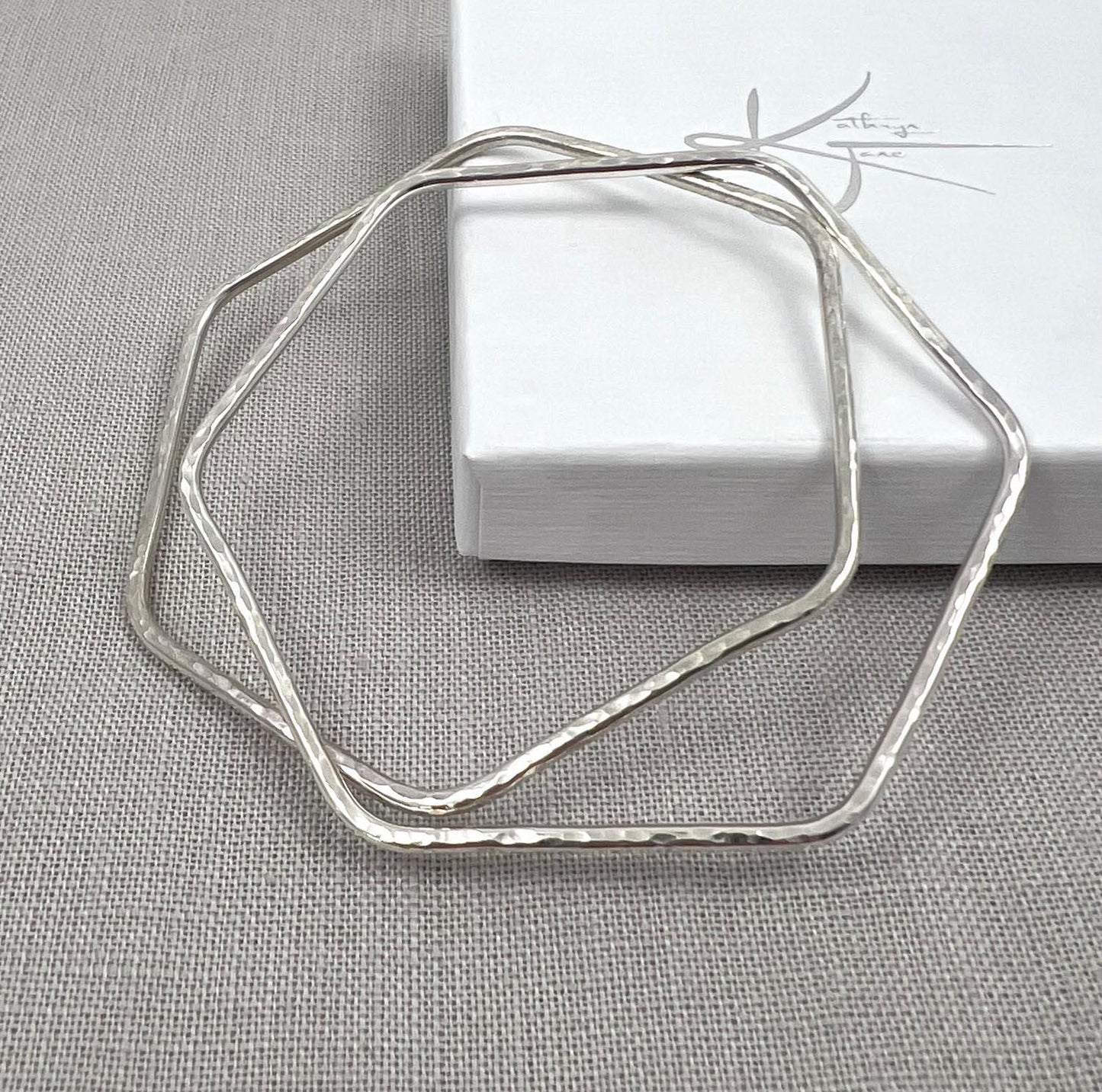 Hammered silver hexagonal bangle bracelet on light fabric, modern minimalist jewelry