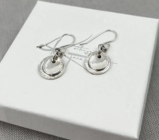 Layered silver dome drop earrings with hammered discs on a white box