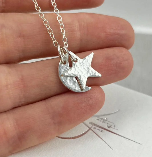 Hand holding silver moon and star hammered charm necklace on delicate chain