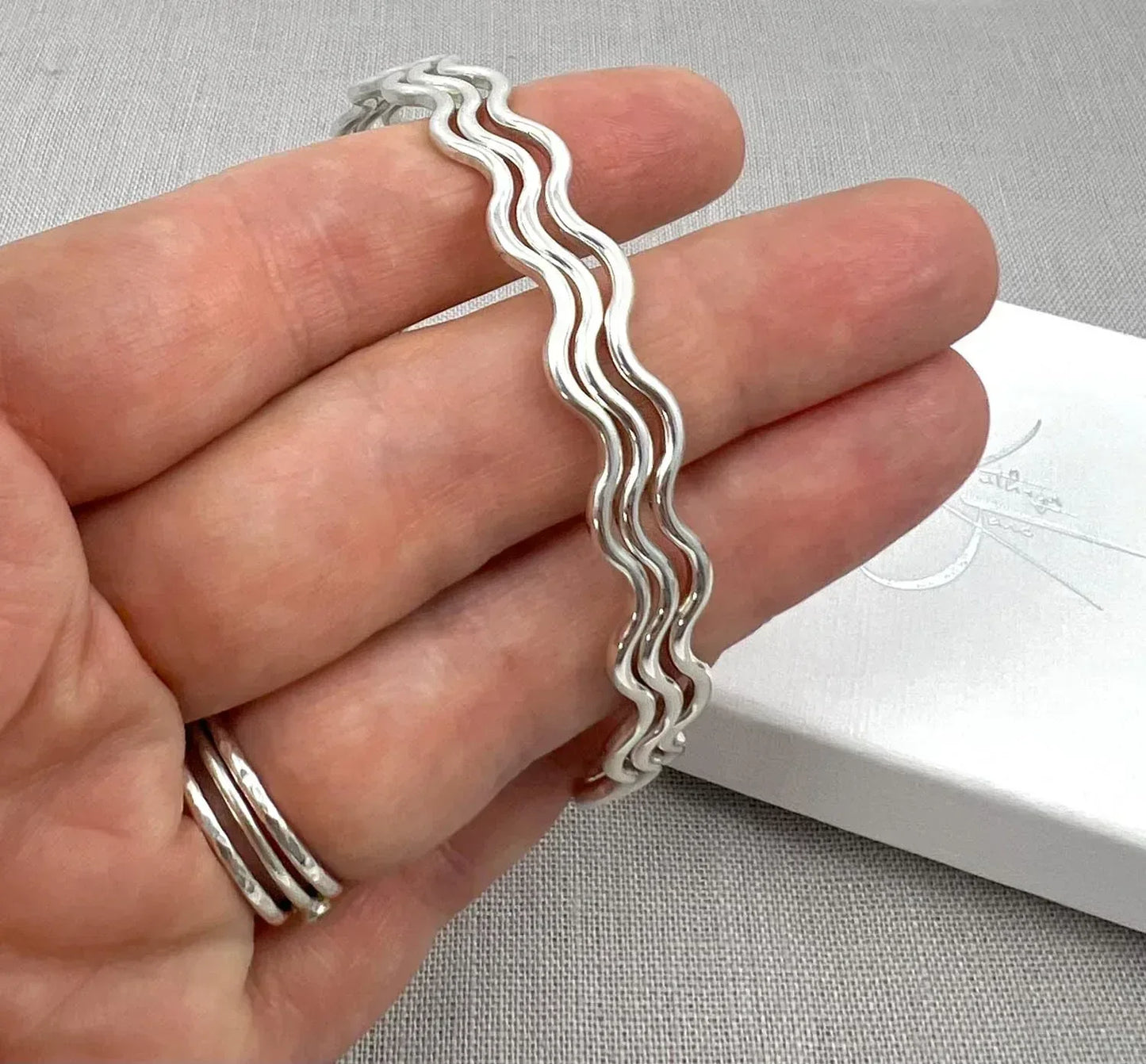 Hand holding a sterling silver wavy bangle bracelet with a textured finish