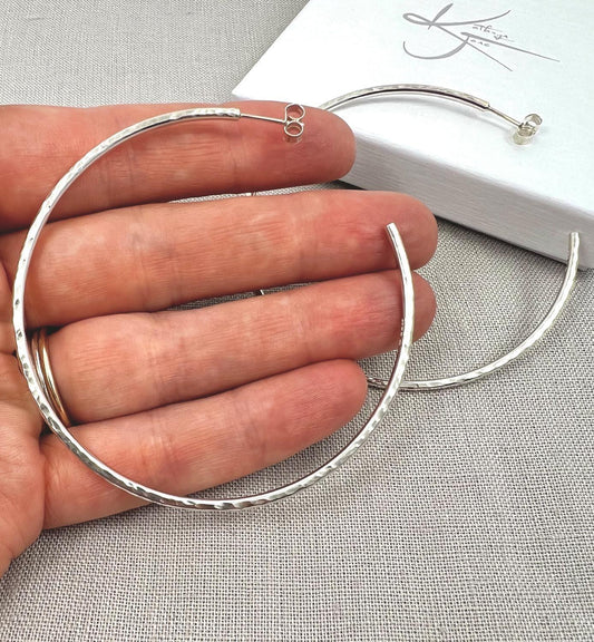 Large hammered silver hoop earrings with stud backs on a neutral fabric background