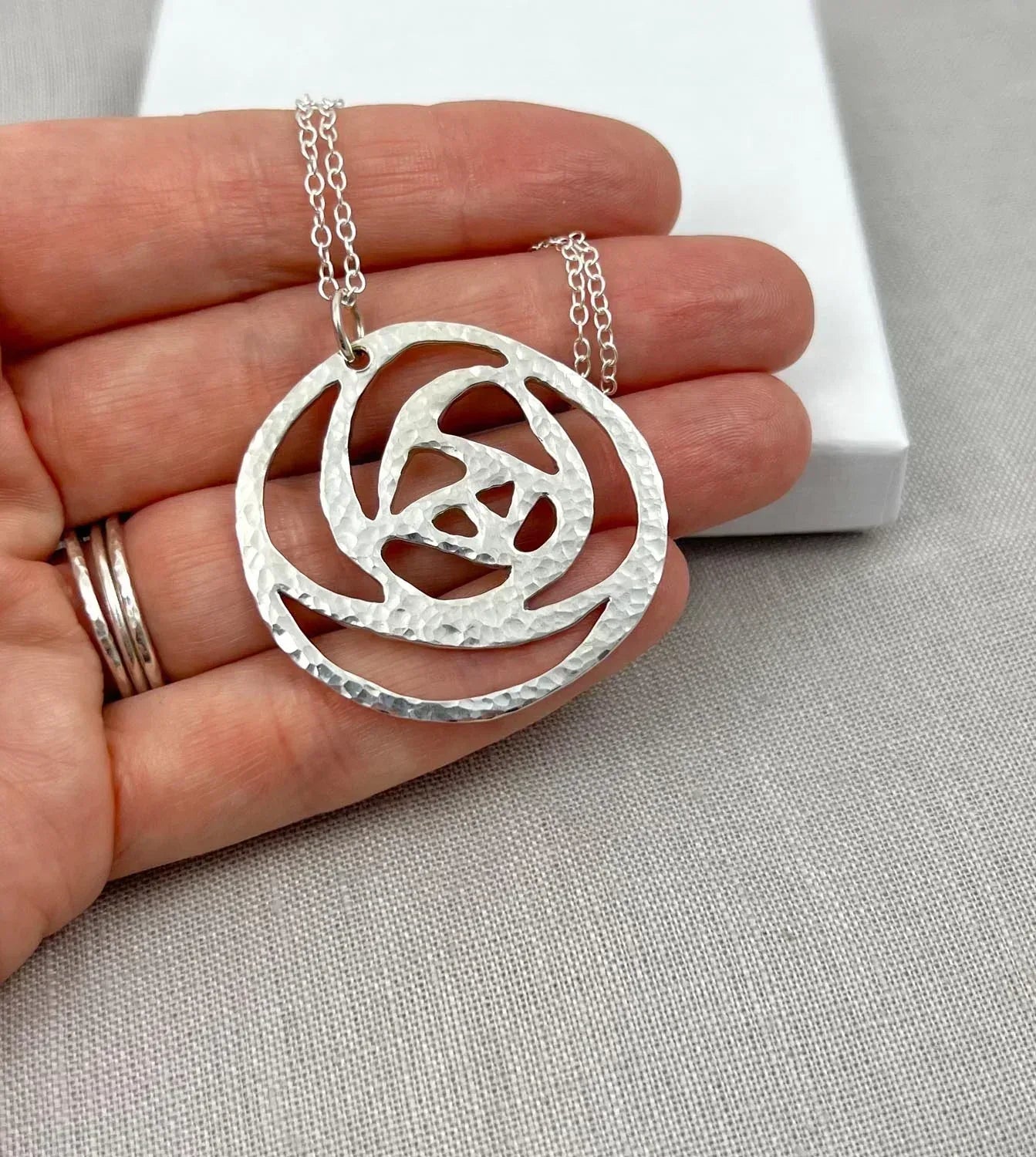 Hand holding a hammered silver rose pendant necklace with a delicate chain