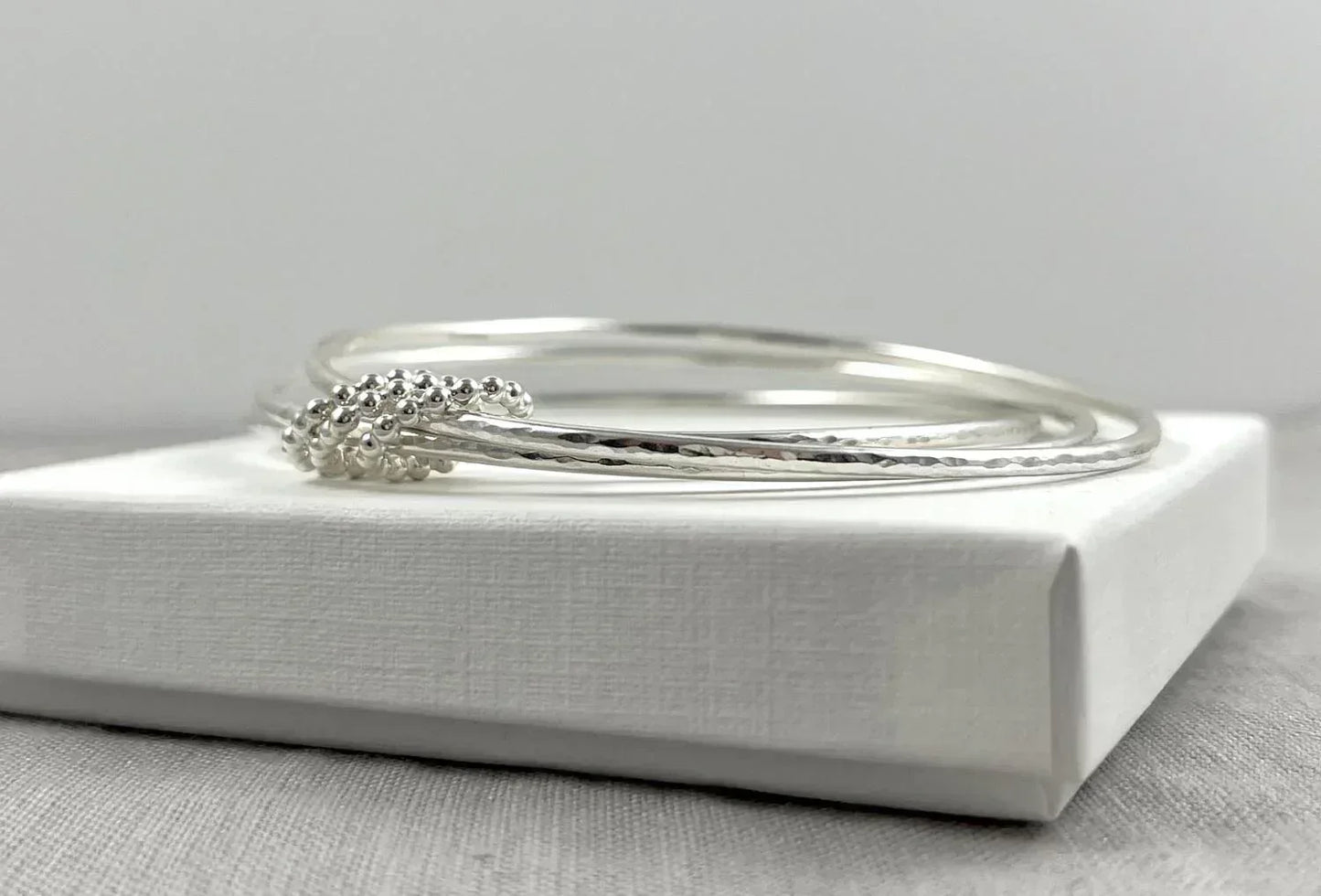 Three linked sterling silver bangles with textured and beaded details on a white box
