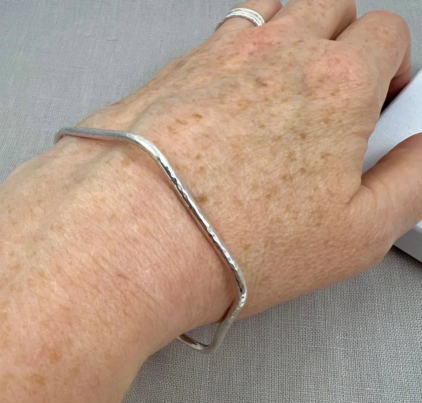 Hand wearing a hexagonal hammered silver bangle on a neutral background