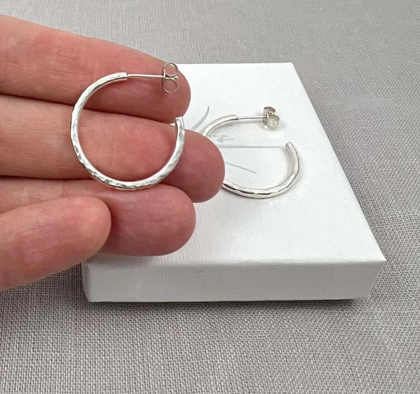 Pair of small hammered silver hoop earrings on a white gift box, textured finish