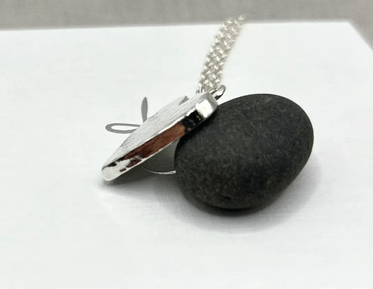 Silver locket necklace with textured pendant displayed on smooth black stone