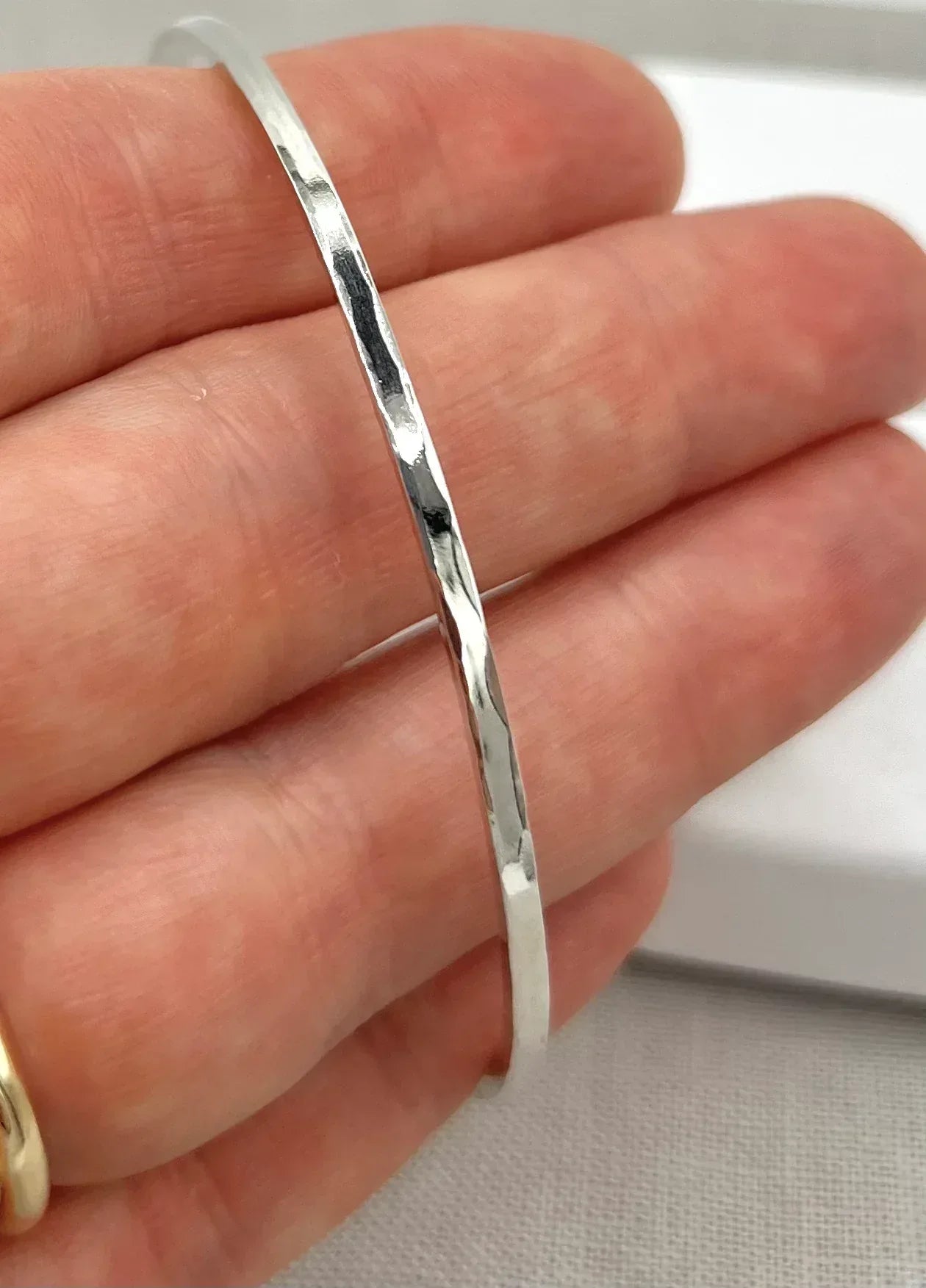Hand holding a lightly hammered sterling silver square wire bangle bracelet