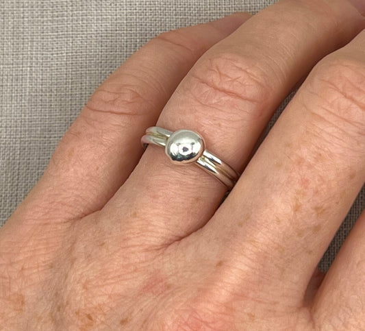 Silver ring with a circular design on a person's finger against a neutral background