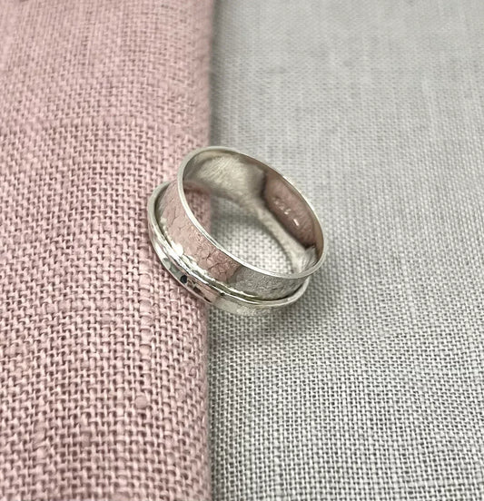 Handcrafted silver spinner ring with a textured band on pink and grey fabric background