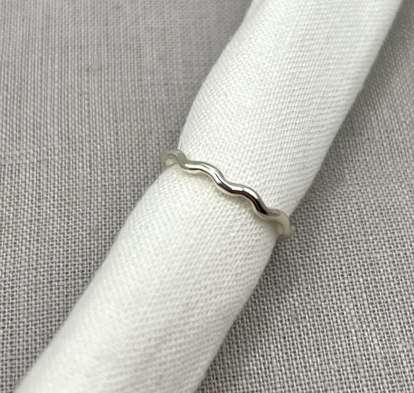 Minimalist silver wavy ring displayed on a white fabric background
