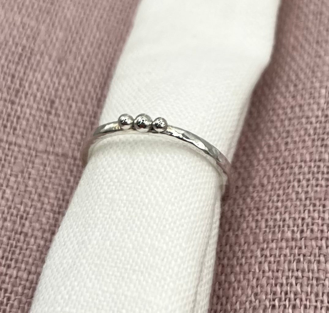 Silver ring with three balls on white linen against a pinkfabric background