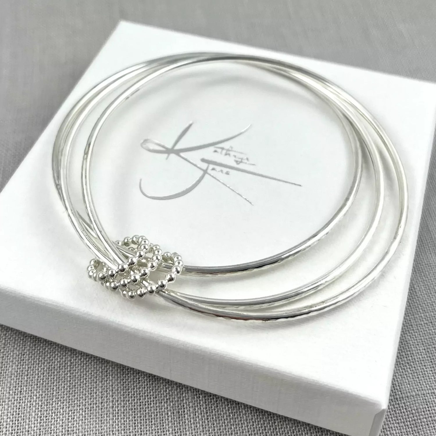 Three silver bangles with beaded accents displayed on a white jewelry box