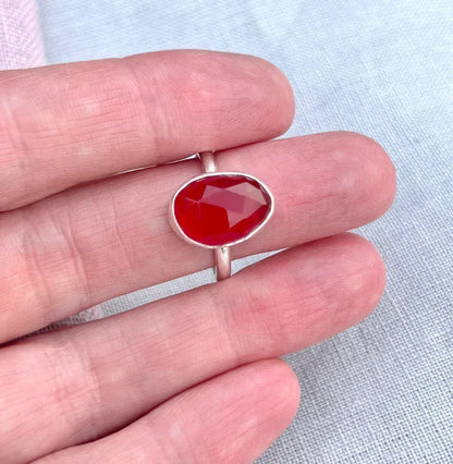 Hand holding a silver ring with a faceted orange gemstone, elegant jewelry design