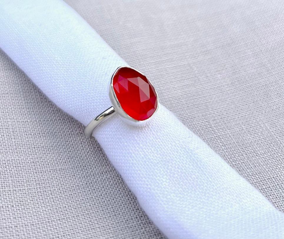 Silver ring with large faceted orange gemstone on white fabric background