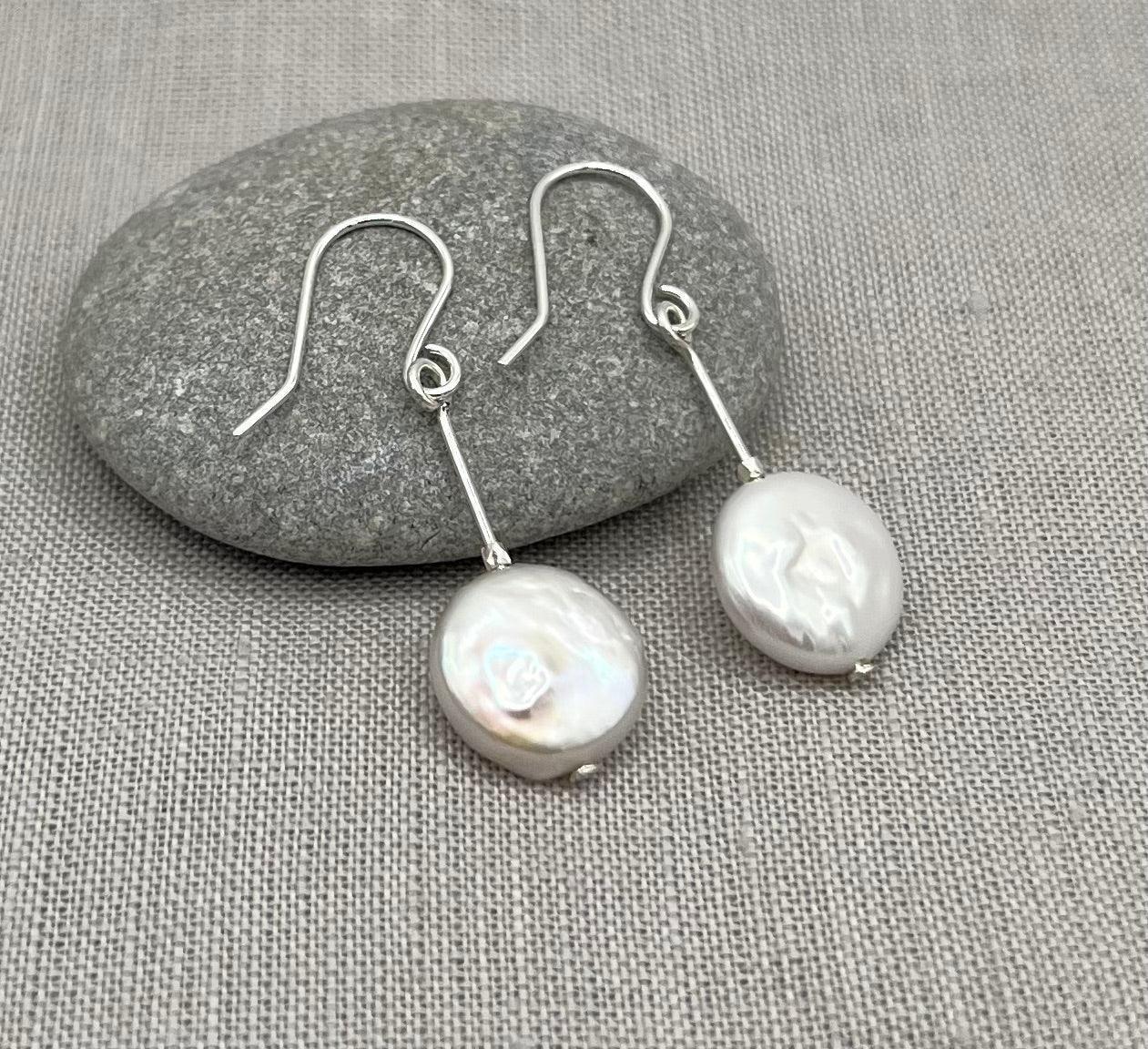 Sterling silver drop earrings with flat coin pearls on linen fabric and grey stone background