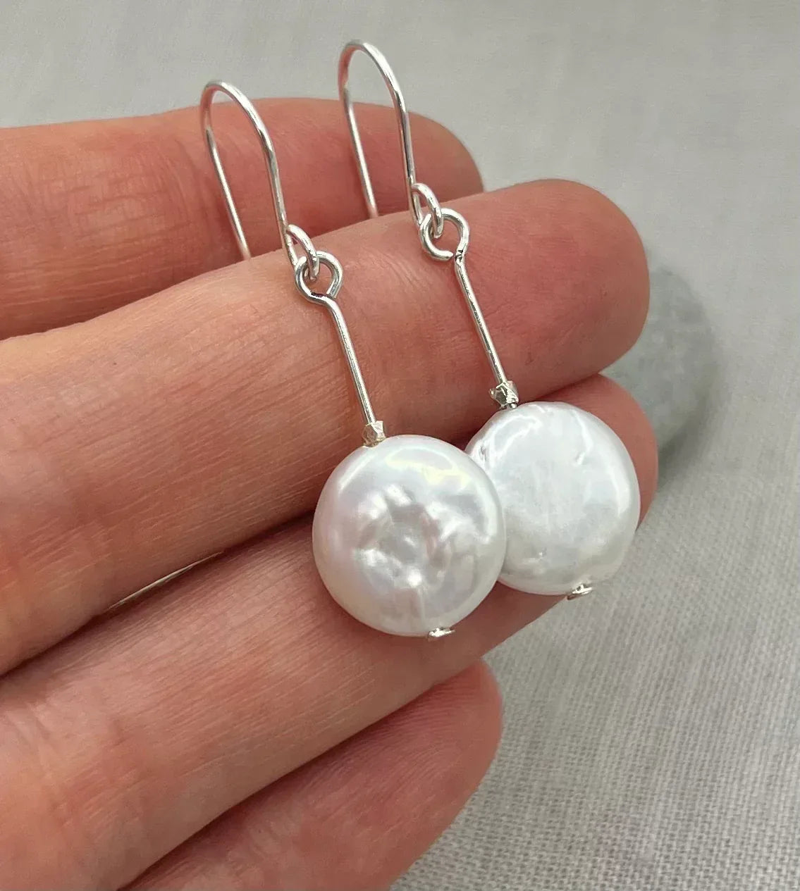 Hand holding silver dangle earrings with round white coin pearls