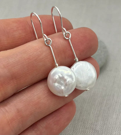 Hand holding silver dangle earrings with round white coin pearls