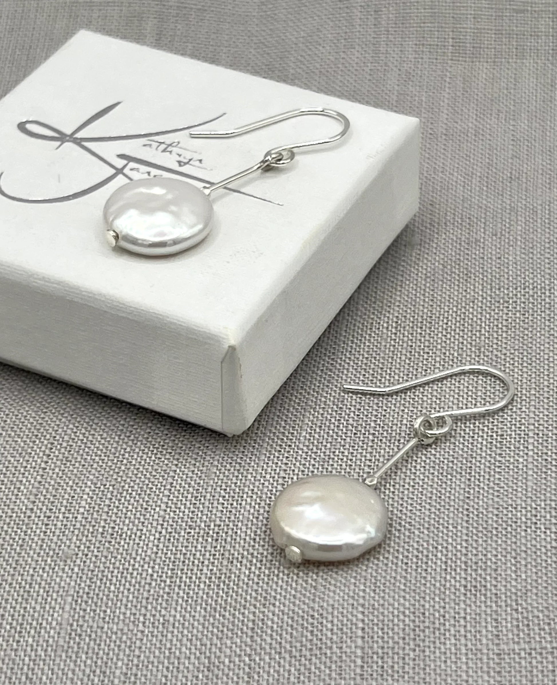Silver drop earrings with round freshwater coin pearls on a fabric background