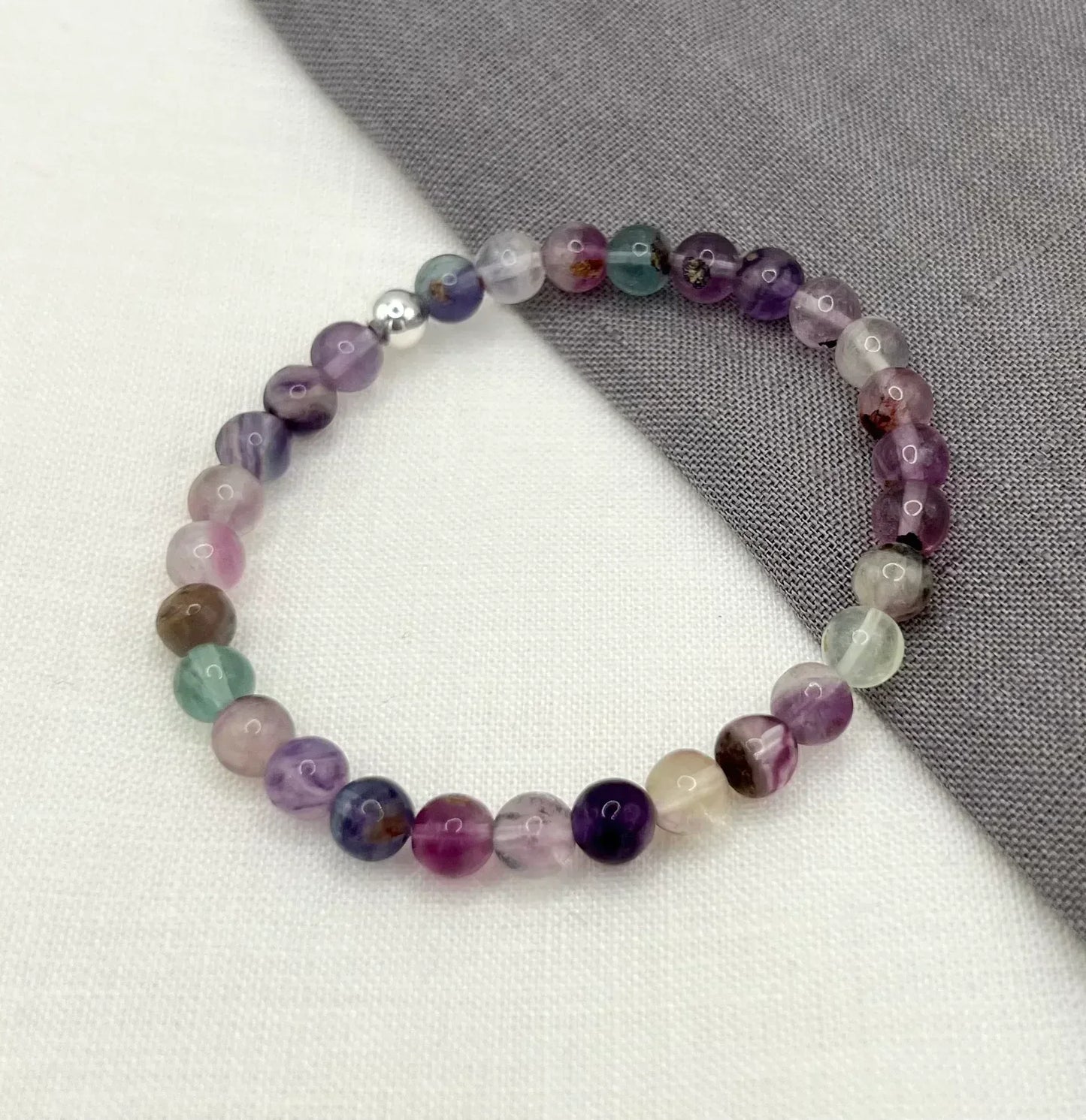 Multicolored fluorite beaded bracelet displayed on white and gray fabric background
