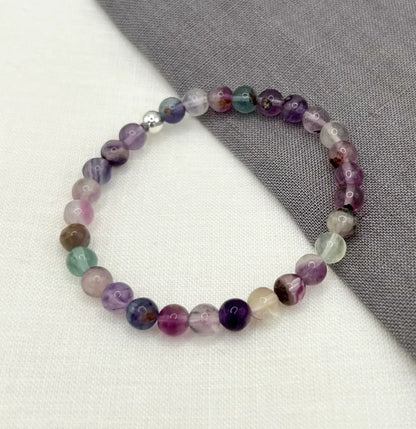 Multicolored fluorite beaded bracelet displayed on white and gray fabric background
