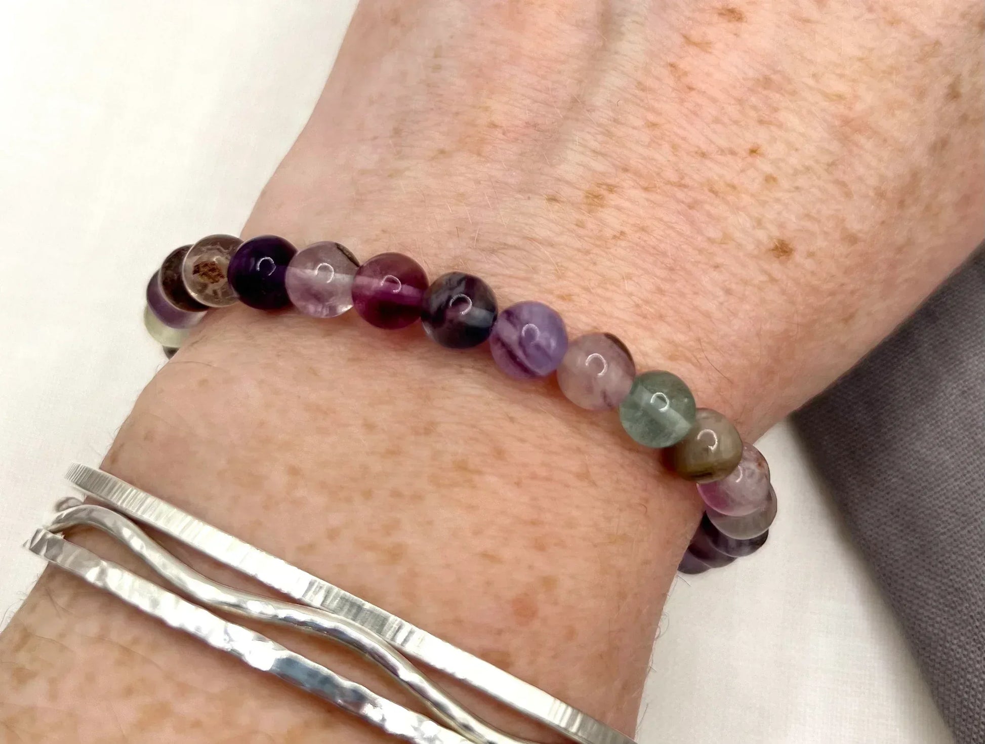 Multicolor fluorite beaded bracelet on wrist with silver bangles, close-up view