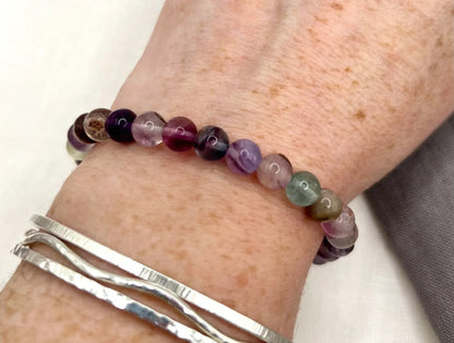 Multicolor fluorite beaded bracelet on wrist with silver bangles, close-up view