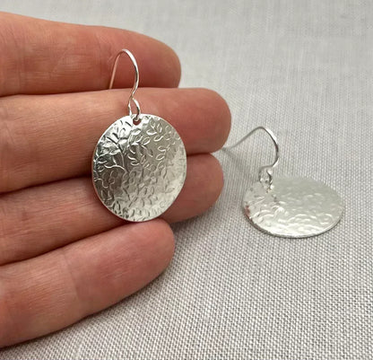 Sterling silver floral disc earrings with textured pattern on linen background