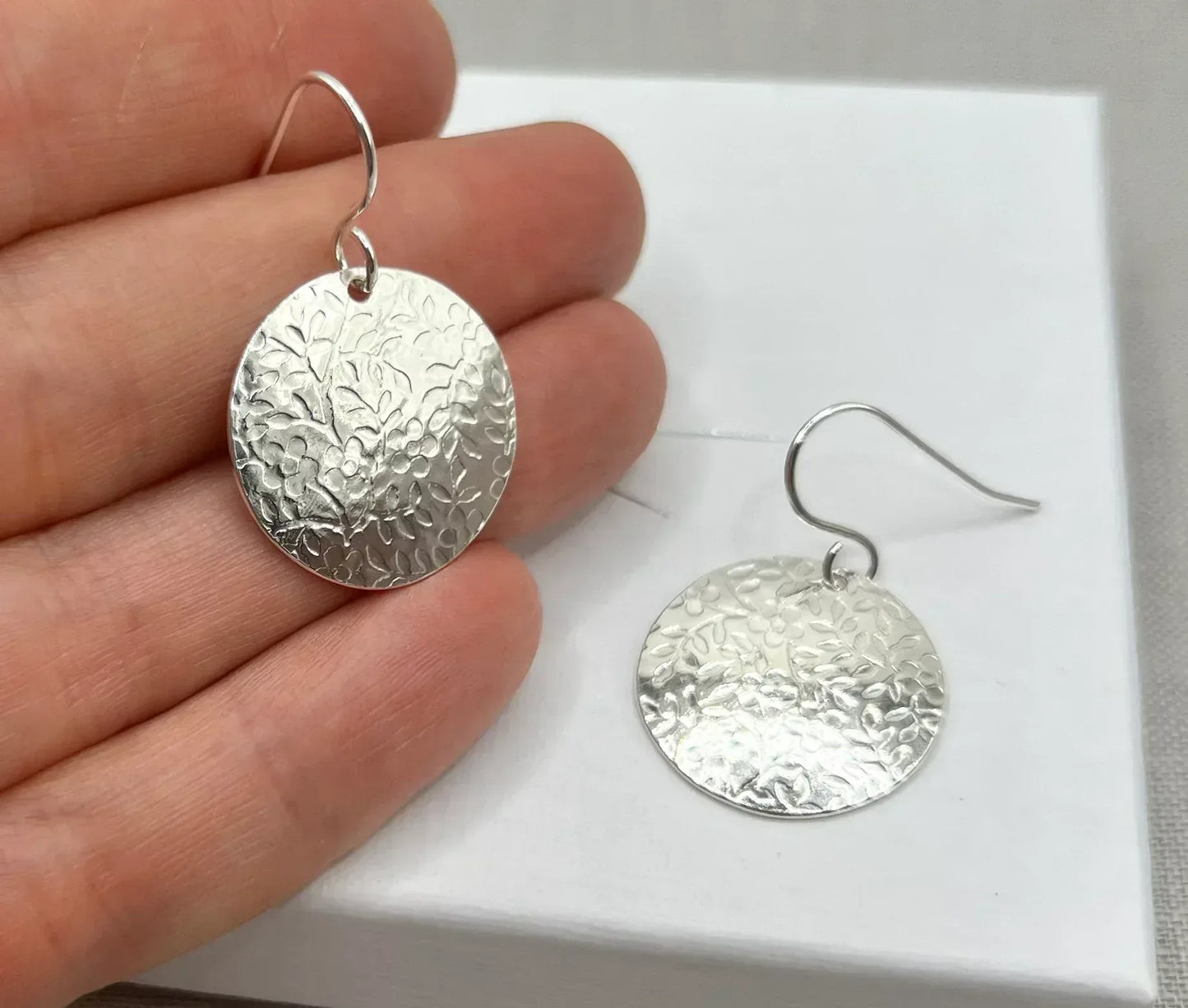 Textured silver disc earrings with floral pattern on a white background