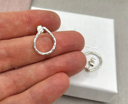 Hand holding a hammered silver teardrop stud earring with another displayed on a box