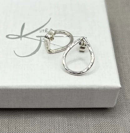 Hammered silver teardrop stud earrings on a white jewelry box, textured finish