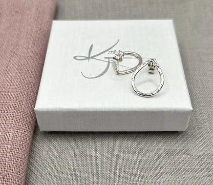 Hammered silver teardrop stud earrings on a white jewelry box with pink and grey fabric background
