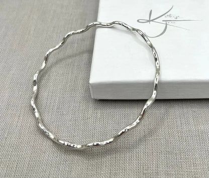 Sterling silver wavy bangle bracelet on light fabric beside a white jewelry box
