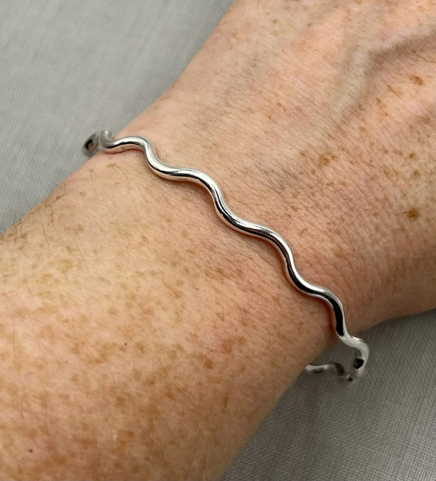 Sterling silver wavy bangle bracelet on wrist, minimalist jewelry design