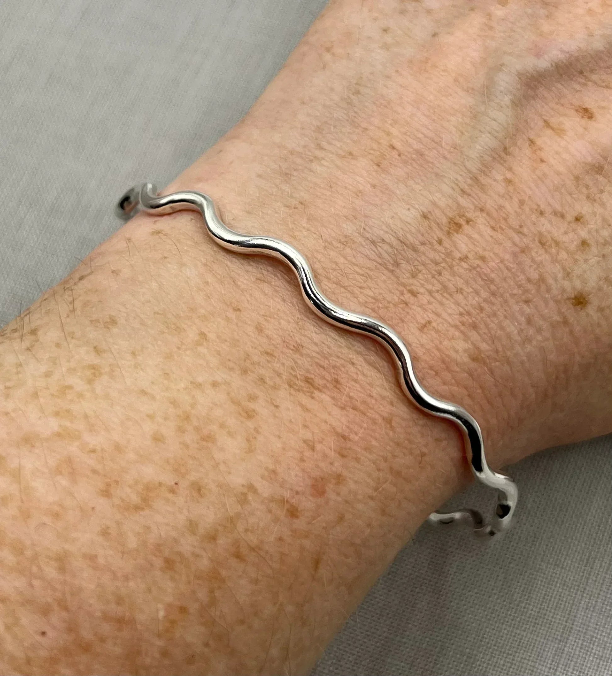 Sterling silver wavy bangle bracelet on wrist, minimalist jewelry design