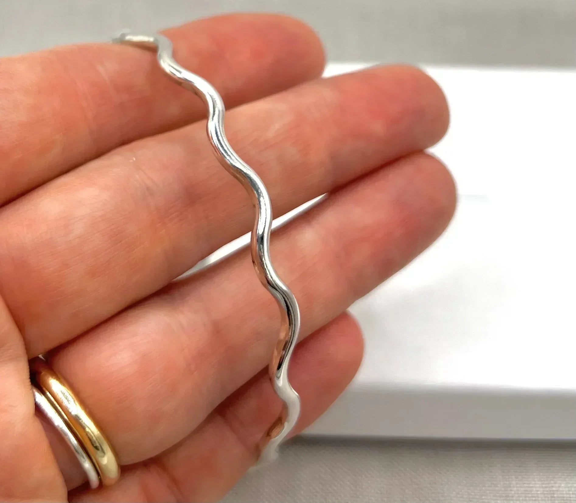 Hand holding a silver wavy bangle bracelet with a polished finish