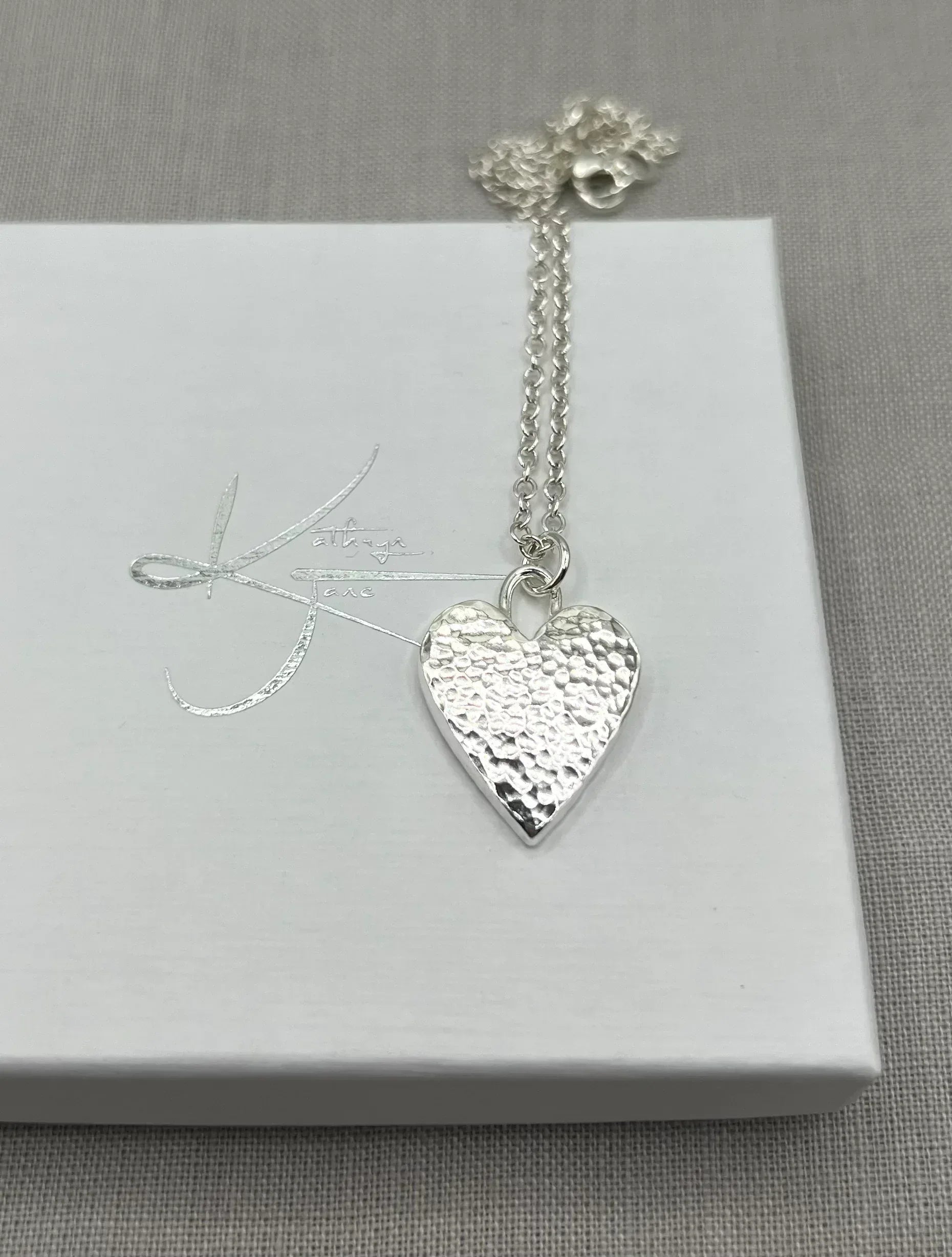 Hammered silver heart pendant necklace on chain, displayed on white jewelry box.