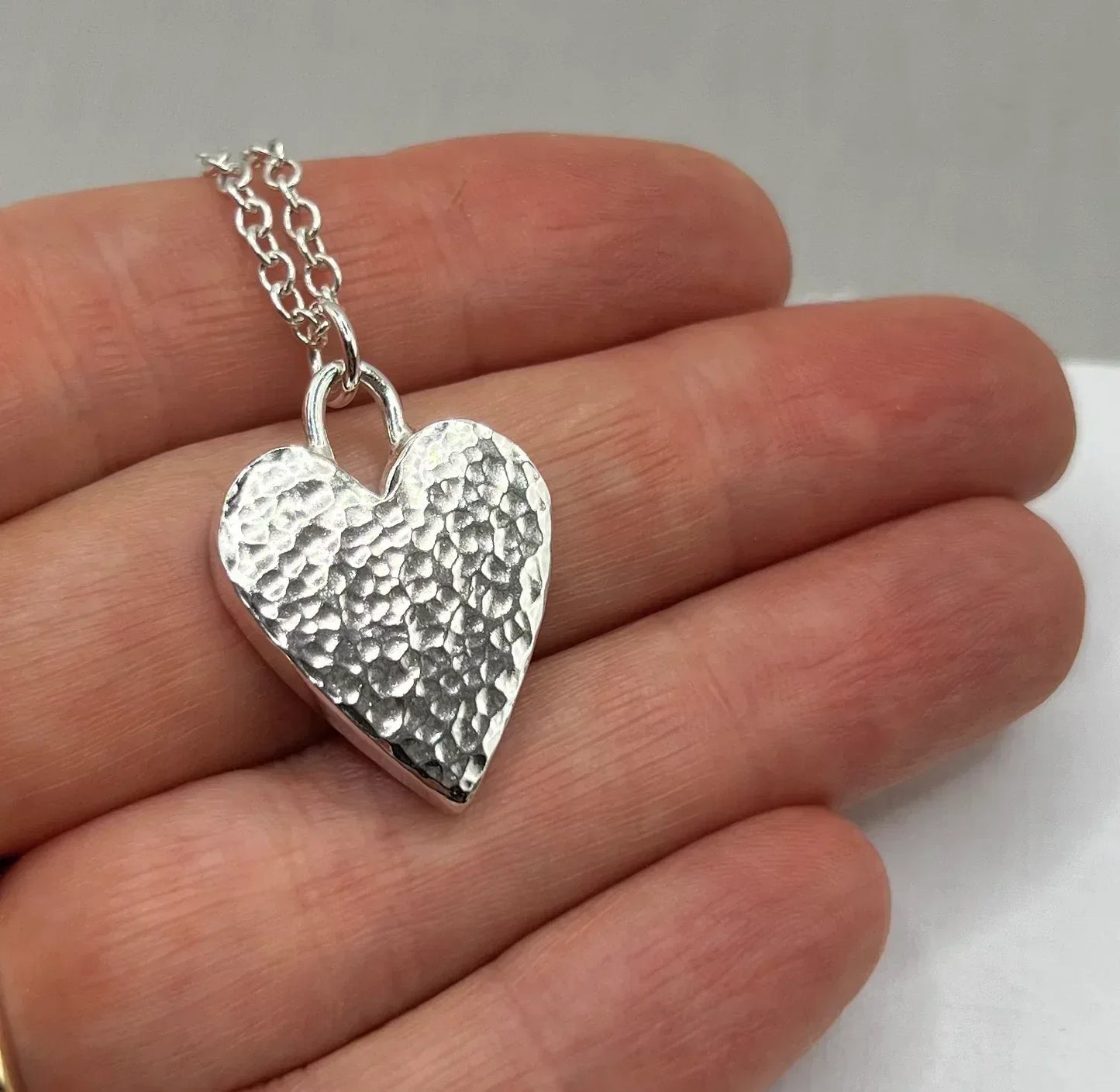 Hand holding a hammered silver heart pendant necklace on a silver chain