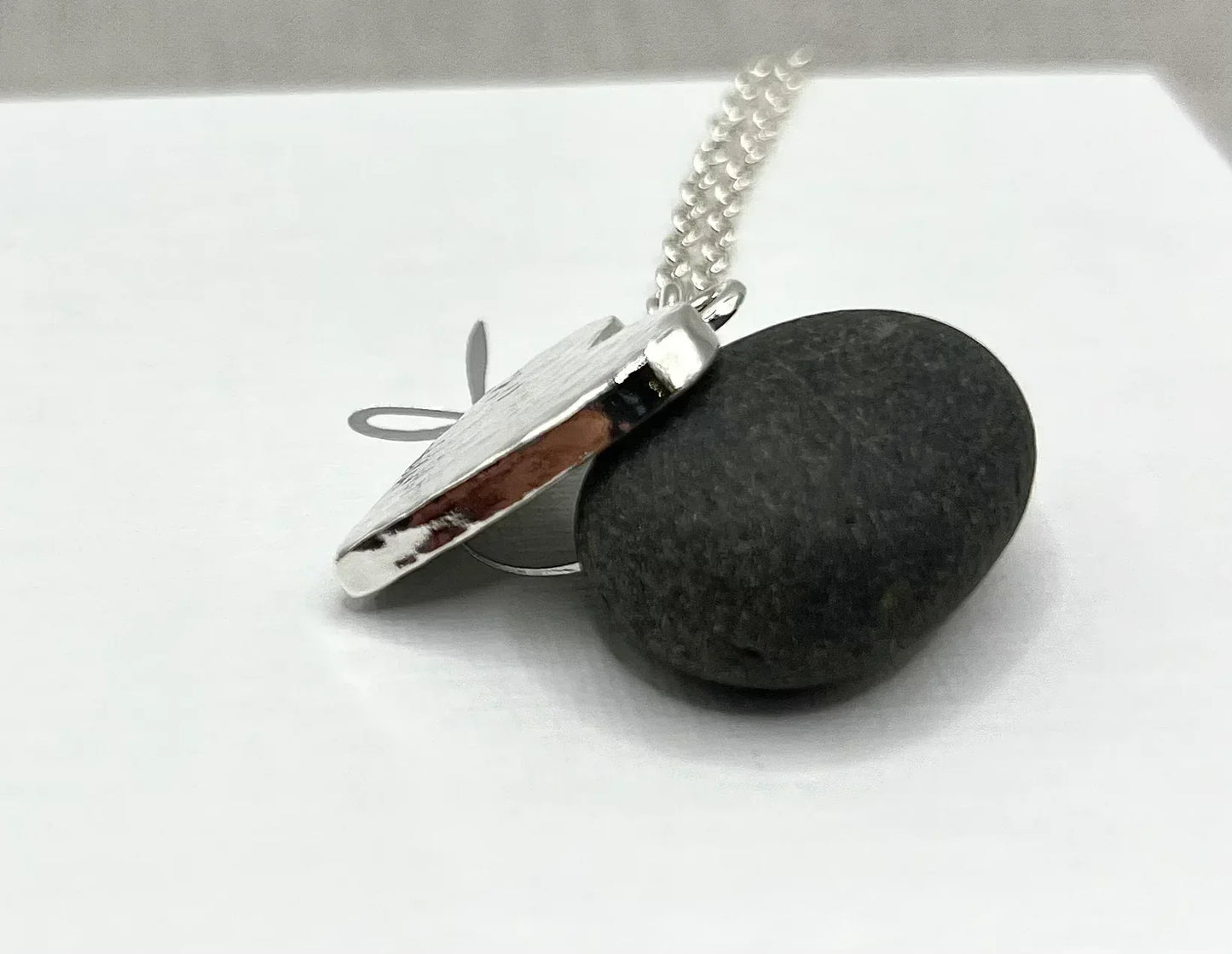 Silver locket necklace with textured pendant displayed on smooth black stone