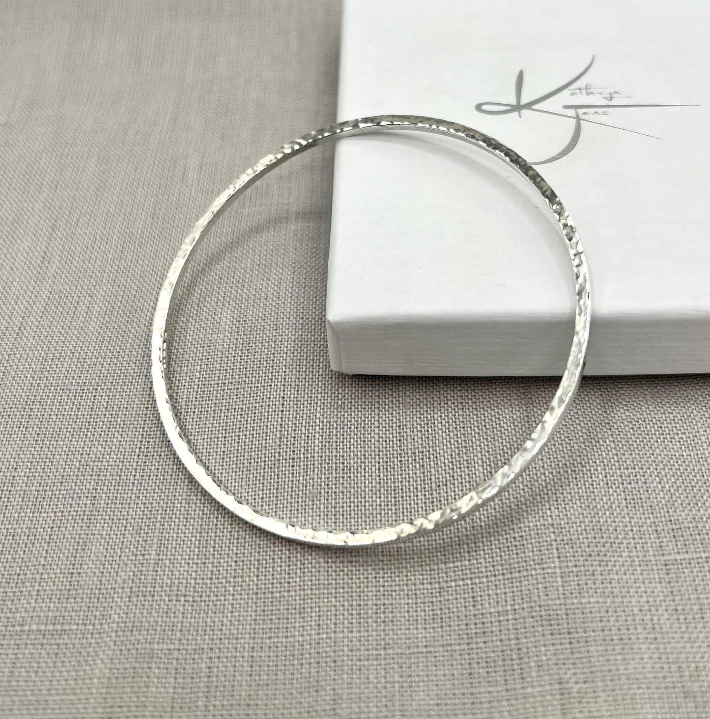 Lightly hammered sterling silver square wire bangle on neutral fabric background