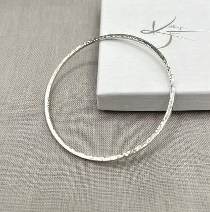 Lightly hammered sterling silver square wire bangle on neutral fabric background