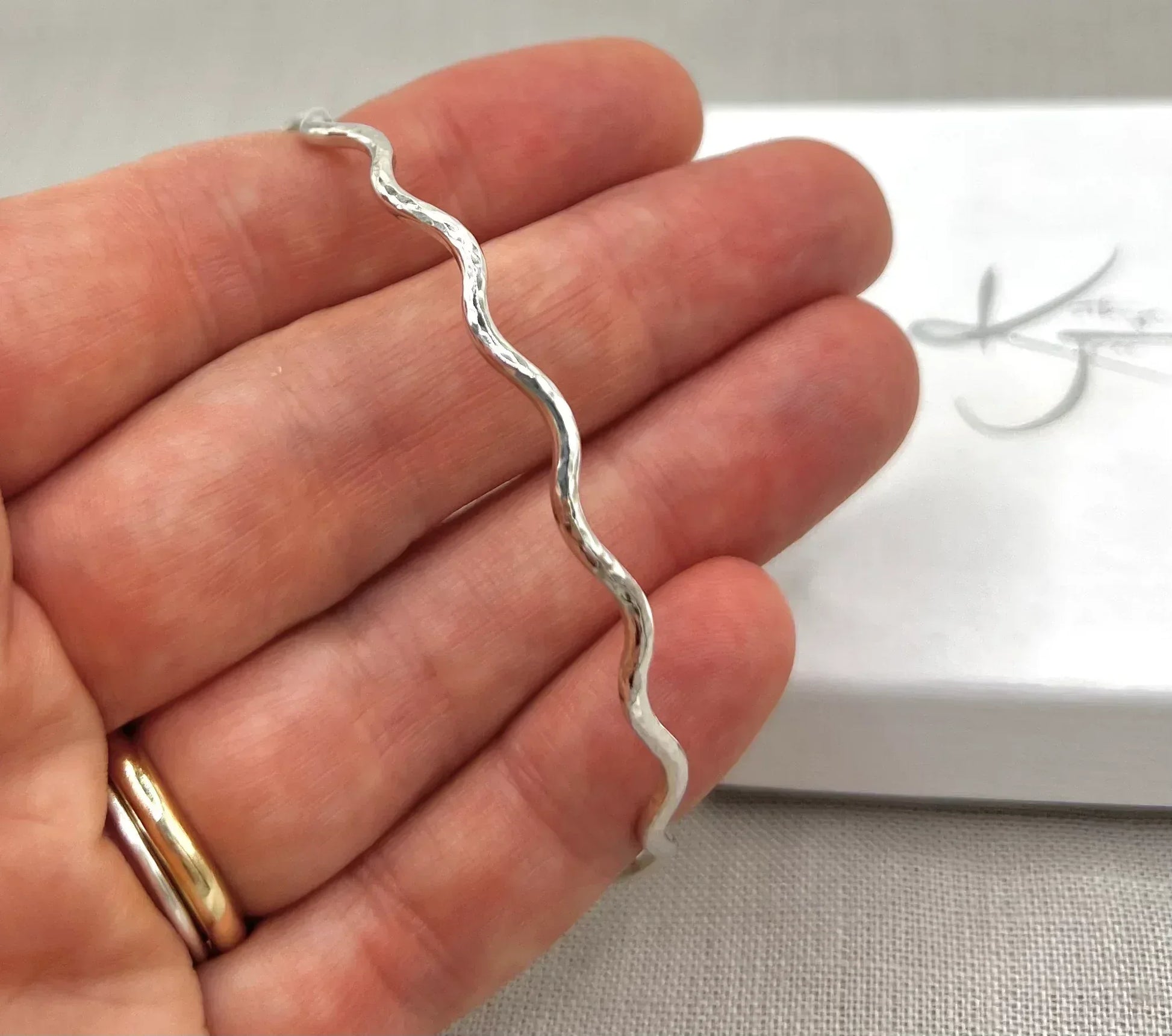 Hand holding a lightly hammered silver wave bangle against a neutral background