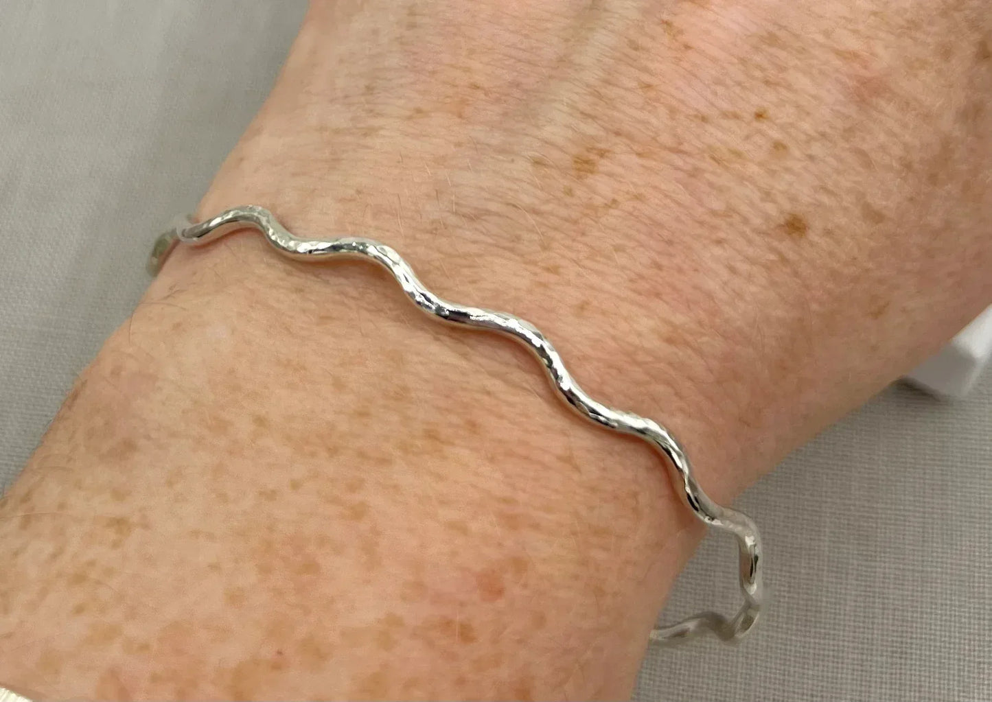 Lightly hammered sterling silver wave bangle bracelet worn on wrist