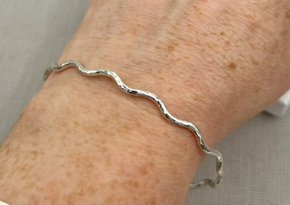 Lightly hammered sterling silver wave bangle bracelet worn on wrist