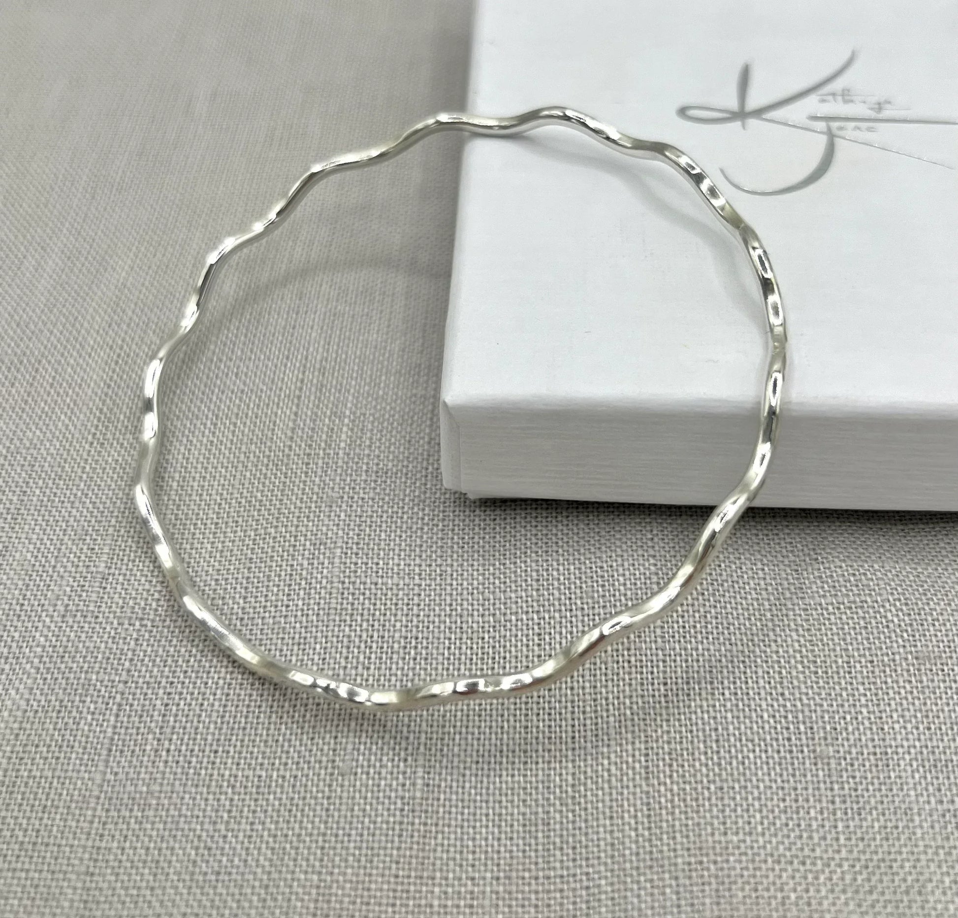 Lightly hammered wavy silver bangle displayed on a neutral fabric background