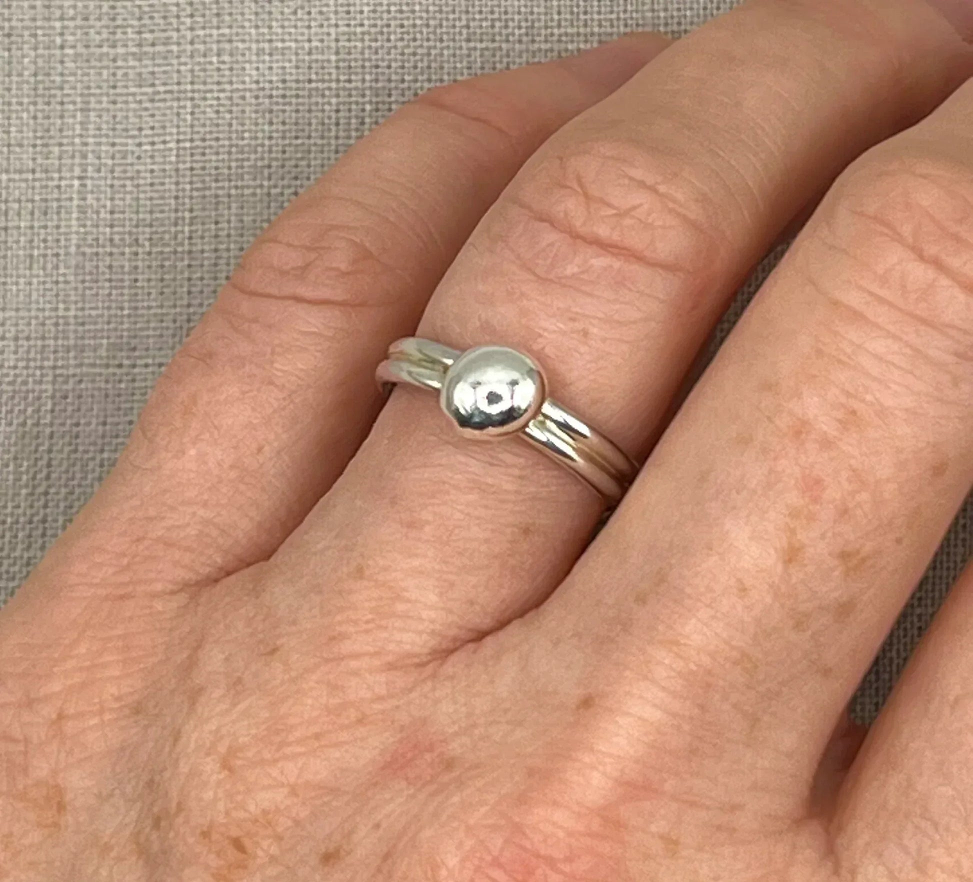 Hand wearing a modern silver double band ring with a polished round nugget accent