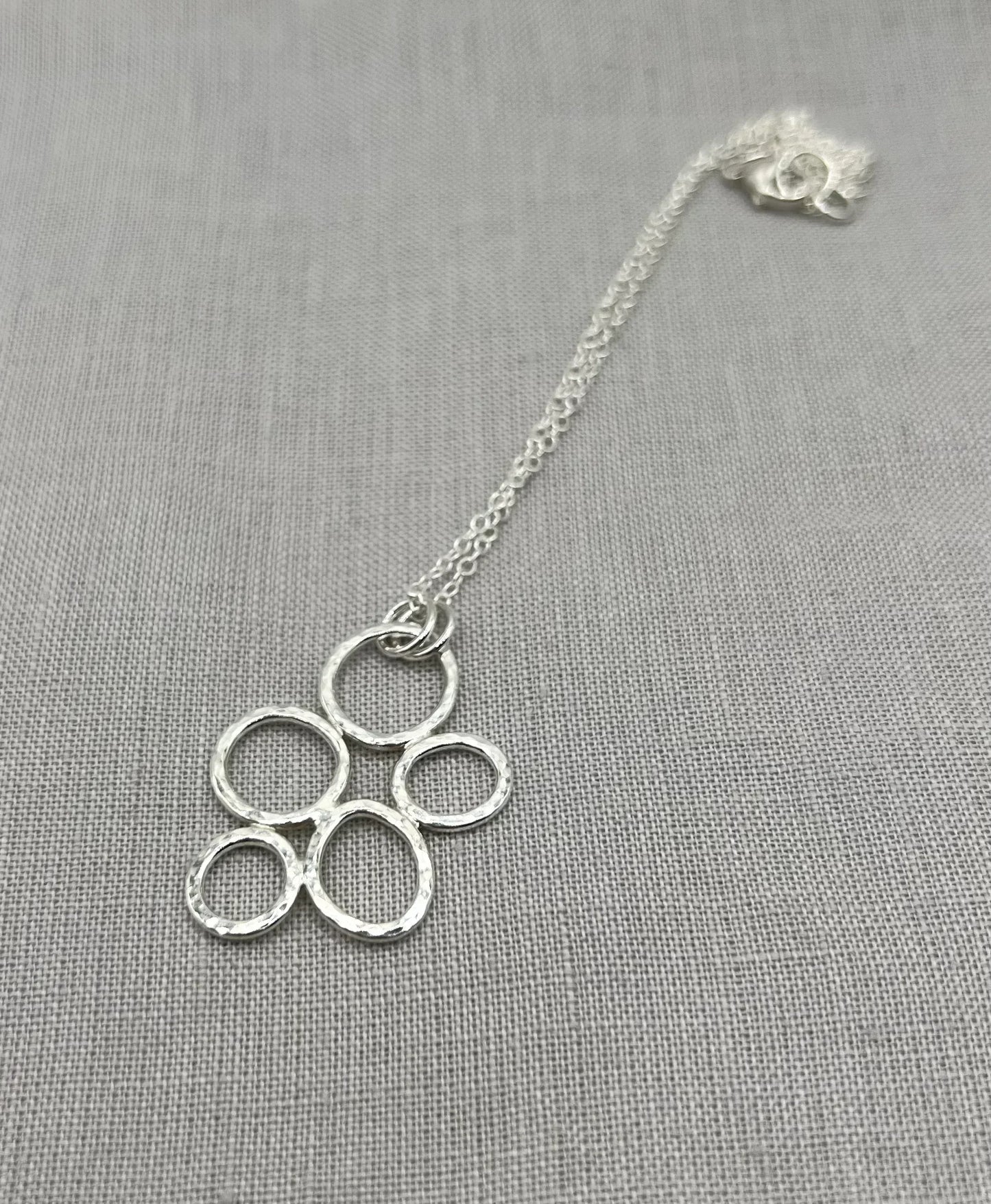 Textured silver pebble necklace with interlinked open circles on a fine chain, on grey fabric.