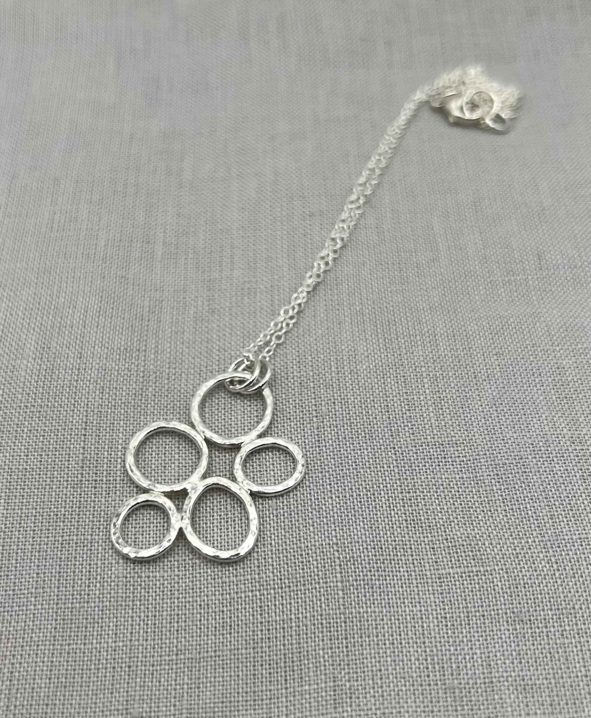 Textured silver pebble necklace with interlinked open circles on a fine chain, on grey fabric.
